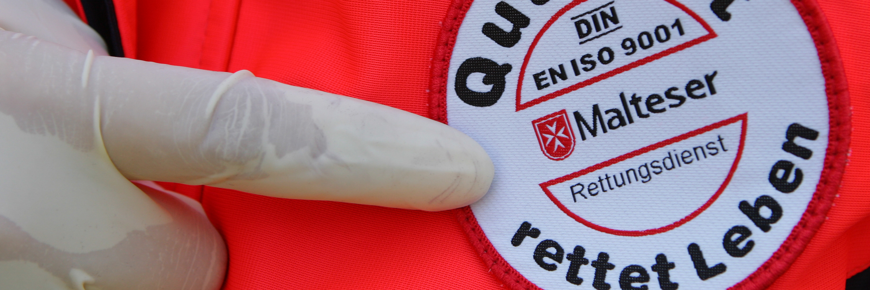 Ein Finger zeigt auf ein Siegel auf dem steht "Qualität rettet Leben". Zu sehen ist das Logo der Malteser.
